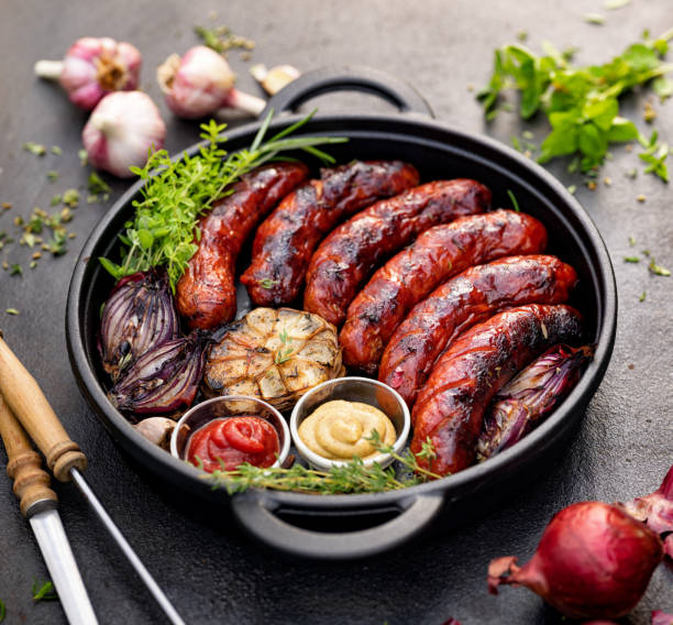 Grilled sausages and vegetables with the addition of ketchup and mustard served in a black cast iron dish stock photo
