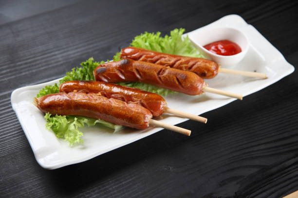 grilled sausages with lettuce and tomato ketchup studio shot of grilled sausages with lettuce and tomato ketchup on black background フランクフルト stock pictures, royalty-free photos & images