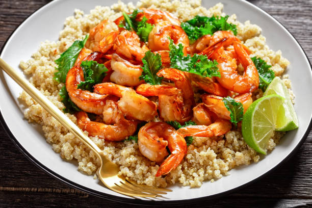 grilled spicy prawns served with sliced avocado and quinoa kale salad on a plate with golden cutlery stock photo