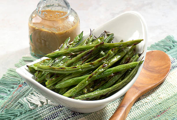 Grilled String Beans Side dish of grilled string beans on table setting. Vinaigrette dressing and wooden spoon runner bean stock pictures, royalty-free photos & images