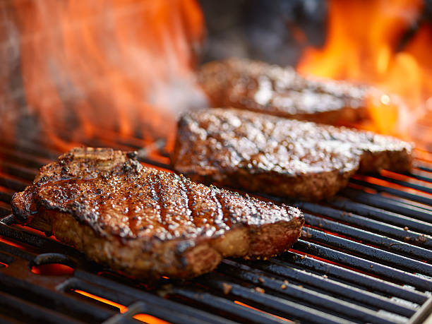 grilling steaks on flaming grill and shot with selective focus - biefstuk stockfoto's en -beelden