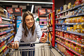 Woman with shopping trolley in supermarket aisle. Buying food in grocery store. Grocery shopping. Beautiful young woman shopping in a grocery store/supermarket