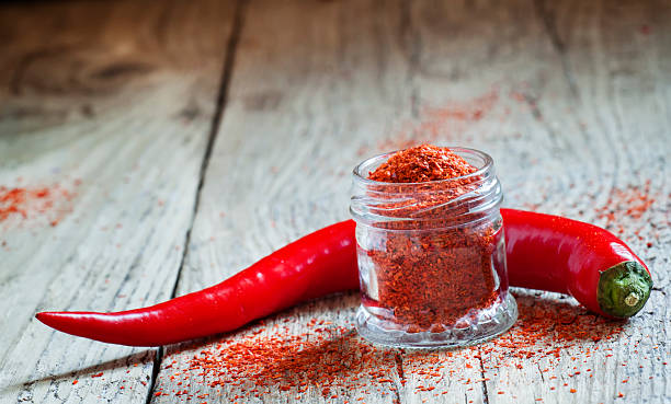 Ground hot red pepper in a glass jar Ground hot red pepper in a glass jar and fresh chili peppers on old wooden background, selective focus cayenne pepper photos stock pictures, royalty-free photos & images