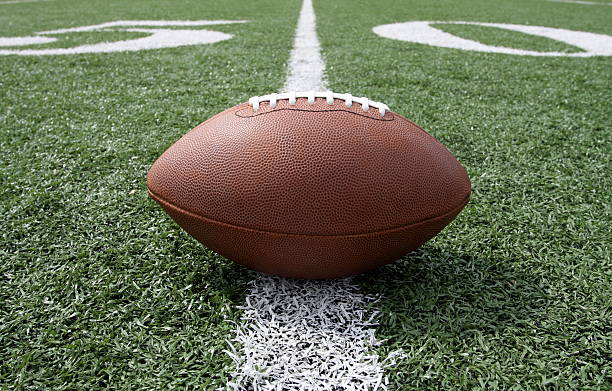 Ground level view of a football on the fifty yard line Football centered and near the fifty yardline american football sport stock pictures, royalty-free photos & images