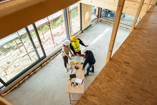 Team of one women architect and two men architects on a construction site. They are looking at blueprint. They are discussing about their project. Shot from above.