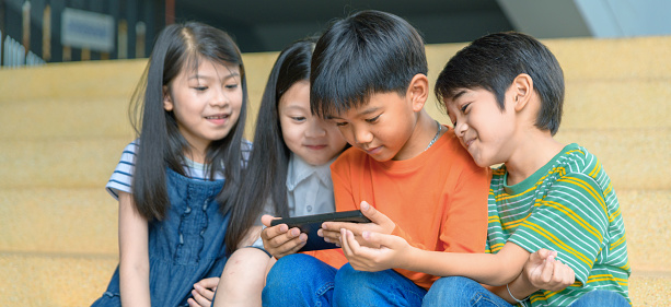 Group Of Asian Kids Play Game On Smartphone Together Smiling Small Brother  And Sister Have Fun
