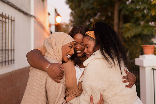 Affectionate female friends embracing each other outdoors. Group of multicultural young women sharing a special moment together. Diverse friends standing on a pavement at sunset.