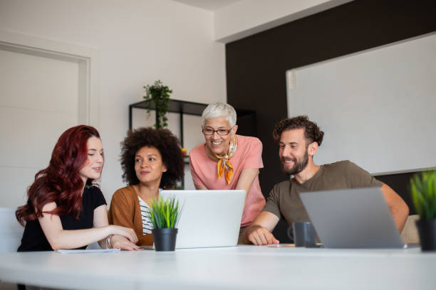 Group of cheerful multi-ethnic colleagues sitting in boardroom and looking at laptop. Group of cheerful multi-ethnic colleagues sitting in boardroom and looking at laptop. multi generation family stock pictures, royalty-free photos & images