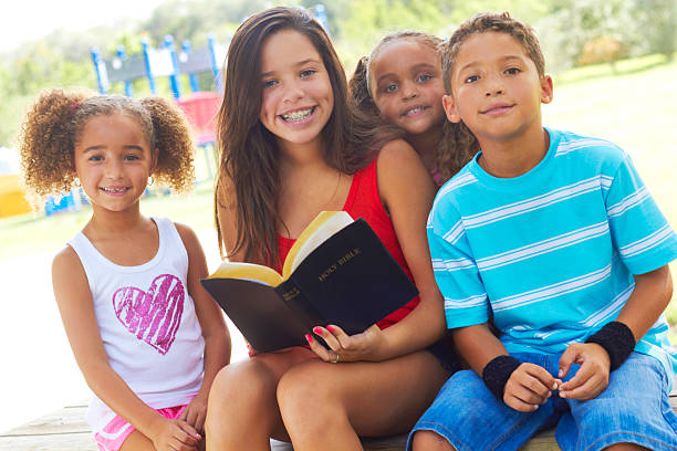 Group of children outdoors around a girl with an open bible stock photo