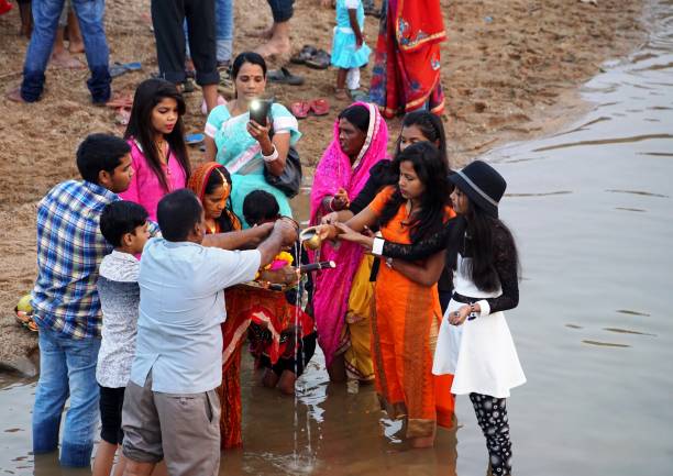 A Group of devotee is making the offerings (Arghya) to the God Sun in river. In the Evening, A Group of devotee is making the offerings (Arghya) to the God Sun in river on the occasion of Chhath. There are many rituals in this chhath festival. The arghya is made in two day. On first day, on the eve of Chhath is mad the offerings (Arghya) to the setting sun and on the final day of Chhath festival, the devotees, along with family and friends, go to the riverbank before sunrise, to make the offerings (Arghya) to the rising sun. According to source Chhath is one of an ancient Hindu Vedic festival of India. The festival is historically native to eastern Uttar Pradesh, North Bihar of India and Mithila State of Nepal. The chhath festival dedicated to the Sun God and his wife Usha (dawn). chhath stock pictures, royalty-free photos & images