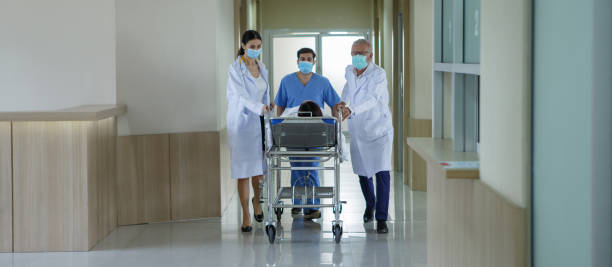 group of diverse doctor and nurse carrying patient on hospital gurney to emergency room in hospital . stock photo