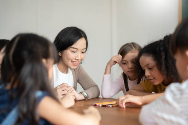 Group of Diverse Pupil playing games with Asian female teacher together in classroom. stock photo