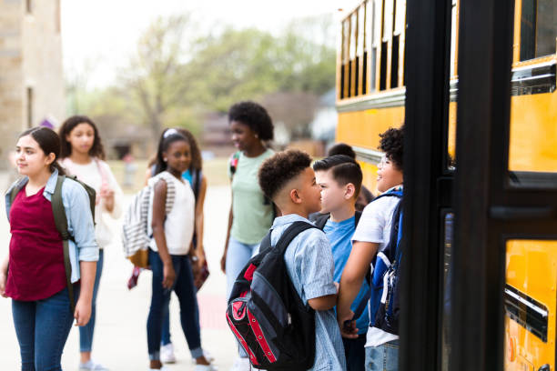 A group of diverse schoolchildren prepare to board school bus Schoolchildren talk with one another before the board a school bus at the end of the school day. boarding schools stock pictures, royalty-free photos & images
