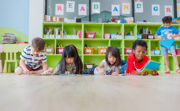 Group of diversity kid lay down on floor and reading tale book in preschool library,Kindergarten school education concept stock photo