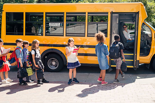 Group of elementary school kids getting in yellow school bus. Group of elementary school kids getting in a yellow school bus. Multi-ethnic group, boys and girls age 8-9, with books, backpack and lunch boxes. A woman is driving the bus, the door is open. Horizontal outdoors shot with copy space. This was taken in Quebec, Canada. boarding school students stock pictures, royalty-free photos & images