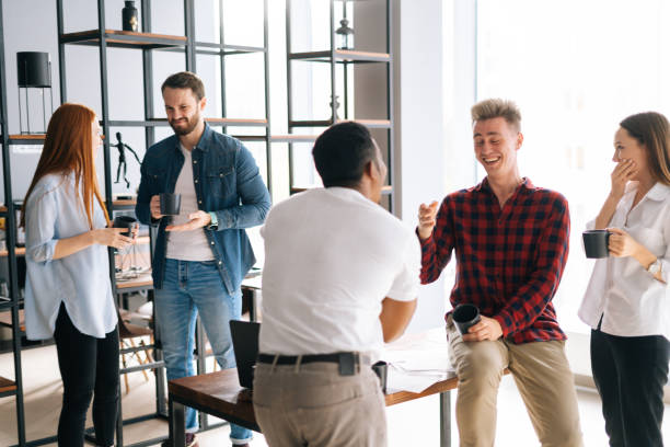 Group of five cheerful young business multi-ethnic startup colleagues enjoying pleasant conversation during coffee break in co-working space. stock photo