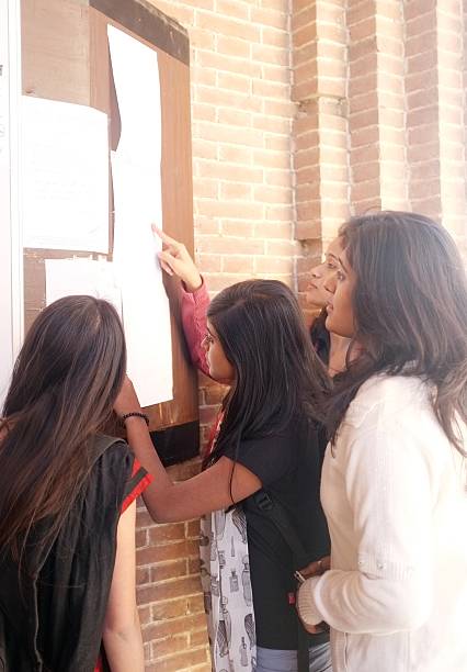 Group of four multi-ethnic students checking their result on board. Team of students reading notice on the bulletin board. students exam results stock pictures, royalty-free photos & images