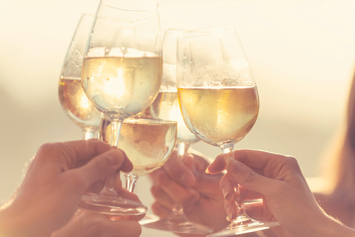 Group of friends drinking wine and making a celebration toast. Tight crop showing wine and hands. Back lit at sunrise or sunset
