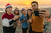 ビーチでクリスマスパーティーを楽しんだり、スマートフォンで自分撮りをする友人のグループ