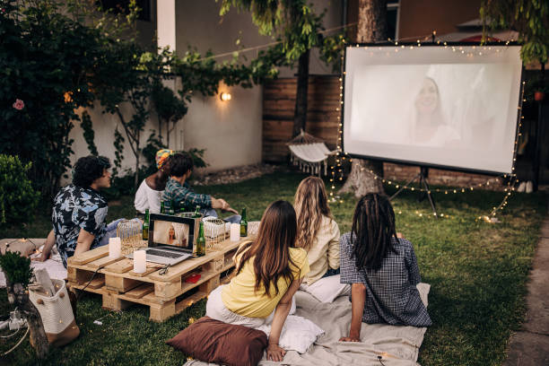Group of friends having a gathering, watching a movie on projector in the garden and hanging out stock photo