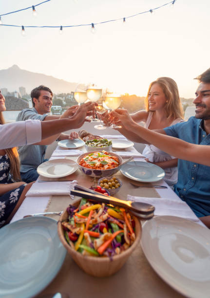 groep vrienden die een maaltijd in openlucht hebben. ze vieren het met een toast met witte wijn. - sunset dining stockfoto's en -beelden