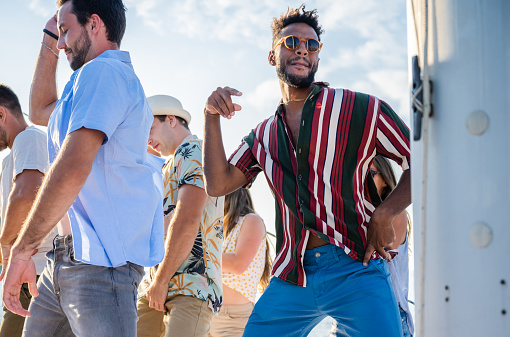 Multiracial millenial friends having fun dancing at sail boat party. Luxury life style concept with young multi ethnic people on sailboat excursion. Happy travel mood.