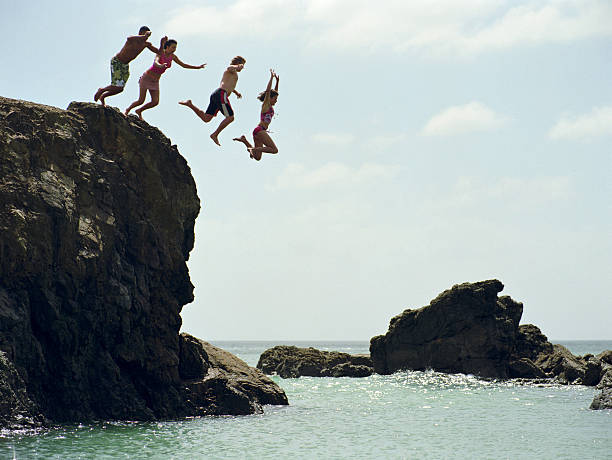 Group of friends jumping into ocean from rock cliff Te Arai Point, North Island, New Zealand. cliff jumping stock pictures, royalty-free photos & images