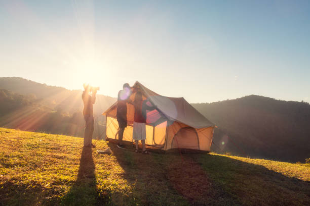 group of friends pitching a tent on campground hill in the sunset - best outdoor tent  個照片及圖片檔