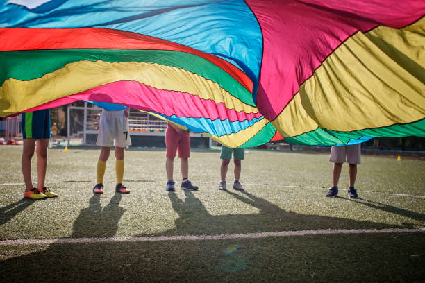 Group of friends playing and waving bright colorful parachute, outdoors party, summer school camp stock photo