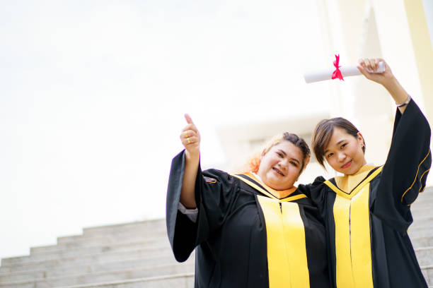 Group of graduated student portrait. Happy Asian young women in the master degree gown showing a diploma in their hand close up. Portrait of confident college students in gown in the graduation ceremony. free degree stock pictures, royalty-free photos & images