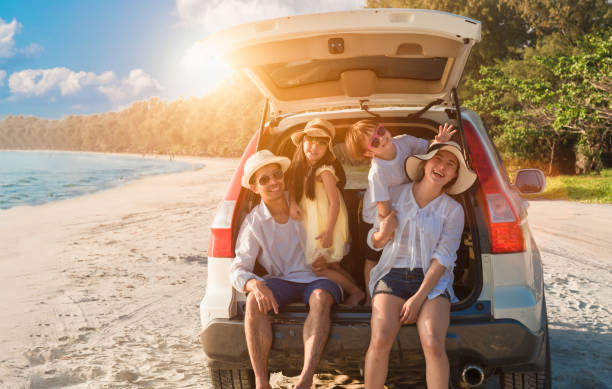 Group of happy Asian family fun travel on road trip in vacation at beach. Father, mother, daughter, son with enjoying on hatchback in seaside in summer holiday. stock photo