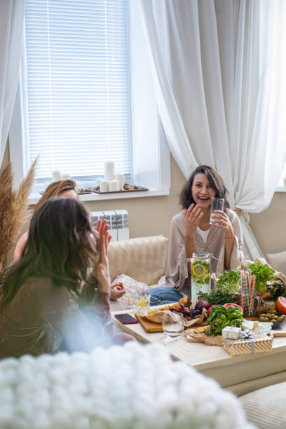 Group of happy female friends talking relaxing together at serving table in boho scandi living room stock photo