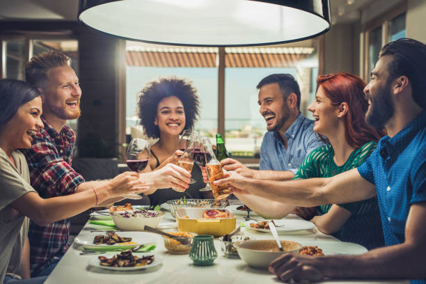 Group of happy friends toasting while eating at dining table. Young cheerful people having fun at dinner party and toasting with alcohol. dinner party stock pictures, royalty-free photos & images