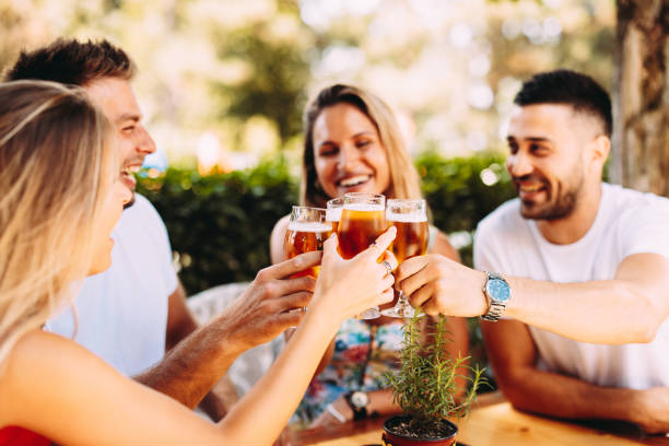Group of happy friends toasting with beer in the backyard at a wooden table. Selective focus on beer stock photo