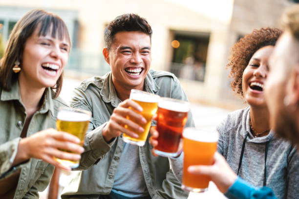Group of happy multiethnic friends drinking and toasting beer at brewery bar restaurant - Beverage concept with men and women having fun together outside stock photo