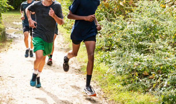 Group of high school boys running on a path A group of high school boys cross country runners are training together on a dirt path in the woods. cross country running stock pictures, royalty-free photos & images