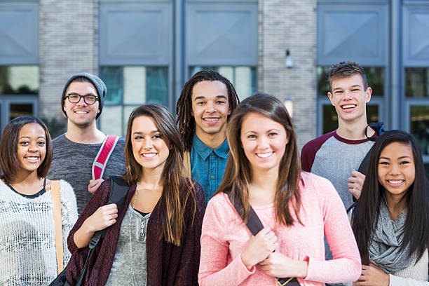 Group of high school or college students A multiracial group of college or high school students standing in front of a school building, carrying bookbags. The woman in the foreground is out of focus. Schools buildings stock pictures, royalty-free photos & images