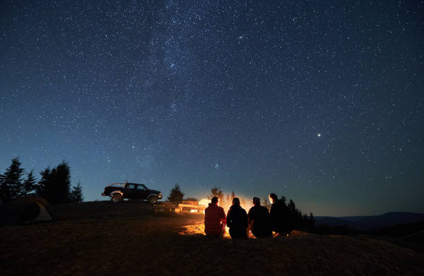 Group of hikers sitting near campfire under night starry sky. stock photo