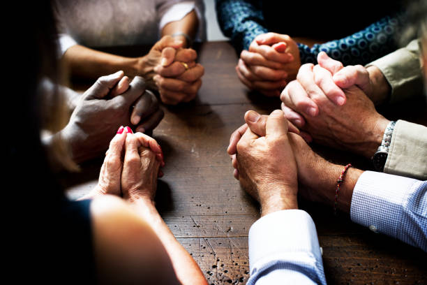 Group of interlocked fingers praying together stock photo