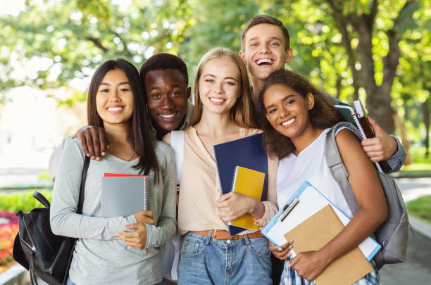 Group of international students having fun after studying Group of international happy students with books and notebooks having fun in park after studying, smiling at camera adolescence stock pictures, royalty-free photos & images