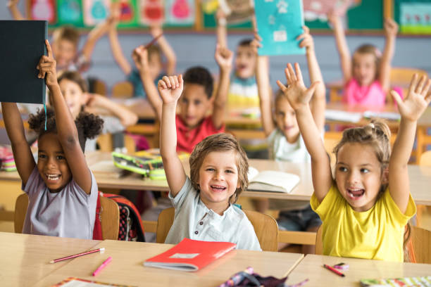 Group of joyful elementary students with raised arms in the classroom. stock photo