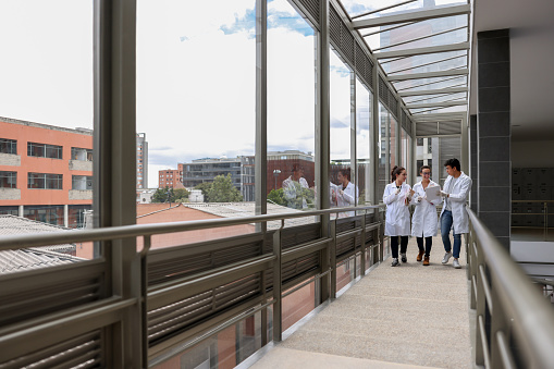 Group of Latin American medical students walking at the university wearing lab coats and talking - education concepts