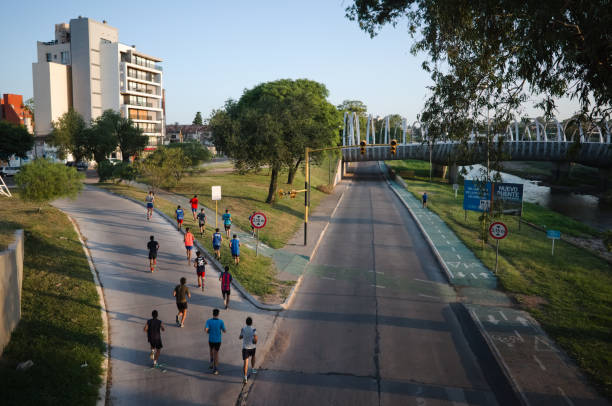 Group of men jogging in evening in residential city area. Male runners group in the park. Modern apartment building, empty road, river and bridge on the background stock photo