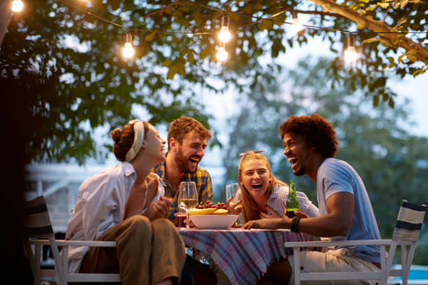 group of multiethnic friends laughing, gathered, talking, sitting at the outdoor table stock photo