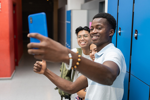 Group of multiracial teenager friends taking photo selfie with phone in the hallway of Secondary School