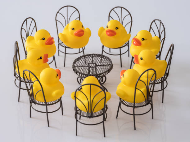 group-of-nine-yellow-rubber-ducks-sitting-on-chairs-facing-each-other-picture-id930034472