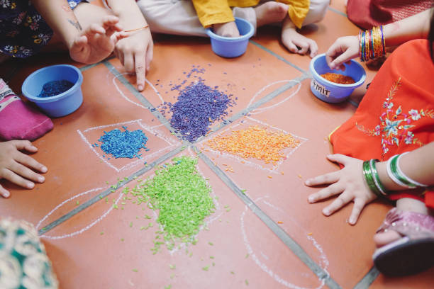 A group of nursery children working together to complete an indian style decoration using coloured rice. stock photo