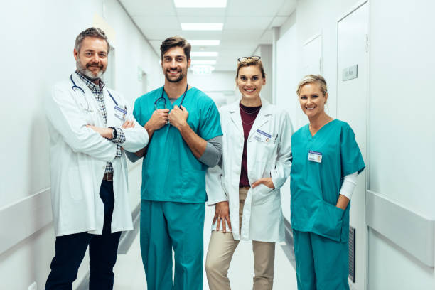Group of paramedics standing in hospital corridor Portrait of positive medical professionals standing in hallway and looking at camera. Group of paramedics smiling in hospital corridor. nurse talking to camera stock pictures, royalty-free photos & images