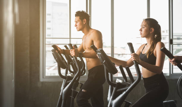 Group of people at the gym exercising on the cross trainer machine. Young fitness men and women doing cardio workout program for beginner. stock photo