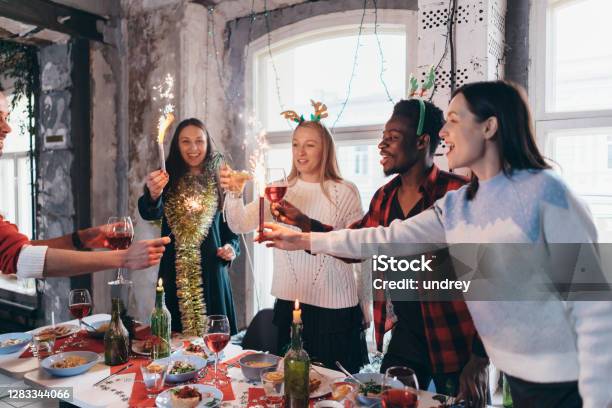 Group of people celebrating Christmas or New Year eve. Friends toasting drinks and enjoying dinner together